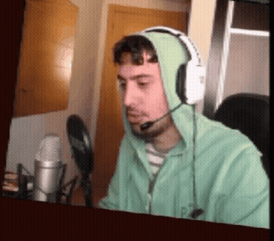 A Man Wearing Headphones And A Green Hoodie Is Talking Into A Microphone . GIF