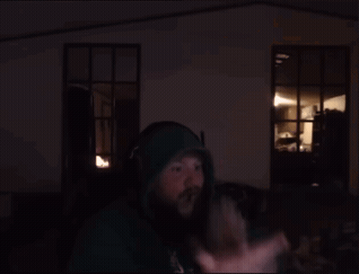 A Man Wearing Headphones And A Green Hoodie Stands In Front Of A Computer Screen GIF