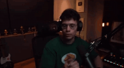 A Man Wearing Headphones And A Green Shirt Is Standing In Front Of A Microphone And Giving The Middle Finger . GIF