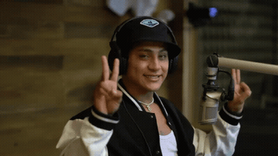 A Man Wearing Headphones And A Hat Giving The Peace Sign GIF