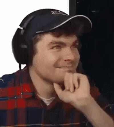 A Man Wearing Headphones And A Hat Is Making A Face . GIF