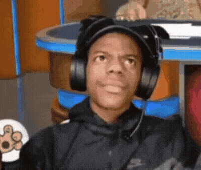 A Man Wearing Headphones And A Hat Is Sitting At A Table GIF