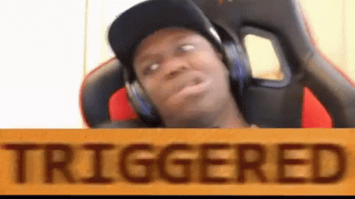 A Man Wearing Headphones And A Hat Is Sitting In A Chair Behind A Sign That Says `` Triggered '' . GIF