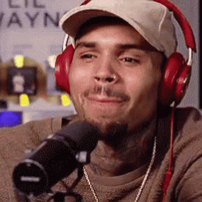 A Man Wearing Headphones And A Hat Is Sitting In Front Of A Microphone . GIF