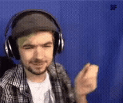 A Man Wearing Headphones And A Hat Is Standing In Front Of A Blue Wall . GIF