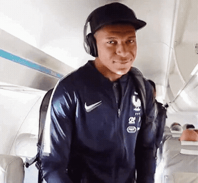 A Man Wearing Headphones And A Hat Is Walking On An Airplane . GIF
