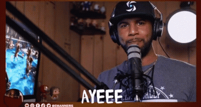A Man Wearing Headphones And A Hat Stands In Front Of A Microphone With The Word Ayeee Above Him GIF