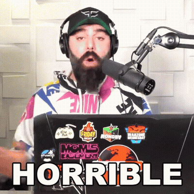 A Man Wearing Headphones And A Hat Stands In Front Of A Microphone With The Word Horrible Written Below Him GIF