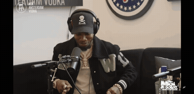 A Man Wearing Headphones And A Hat With A Skull And Crossbones On It Talks Into A Microphone GIF