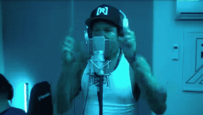A Man Wearing Headphones And A Hat With The Letter R On It Is Singing Into A Microphone GIF