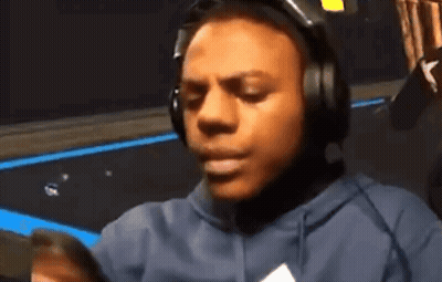 A Man Wearing Headphones And A Hoodie Looks At His Phone GIF