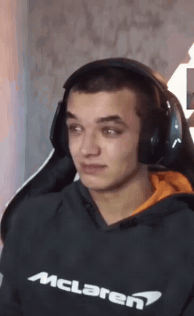 A Man Wearing Headphones And A Mclaren Sweatshirt Is Sitting In A Chair . GIF