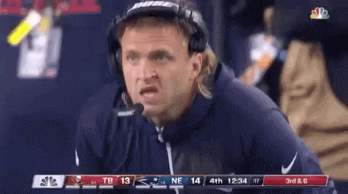 A Man Wearing Headphones And A Microphone Is Sitting On The Sidelines During A Football Game . GIF