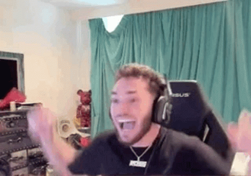 A Man Wearing Headphones And A Necklace Is Sitting In A Chair In A Room . GIF