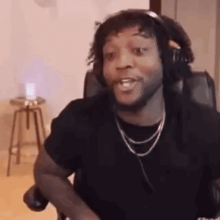 A Man Wearing Headphones And A Necklace Is Sitting In A Chair Making A Funny Face . GIF