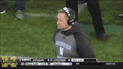 A Man Wearing Headphones And A Northwestern Shirt Watches A Football Game GIF