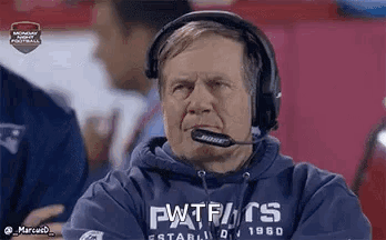 A Man Wearing Headphones And A Patriots Sweatshirt Is Sitting On The Sidelines Watching A Football Game . GIF
