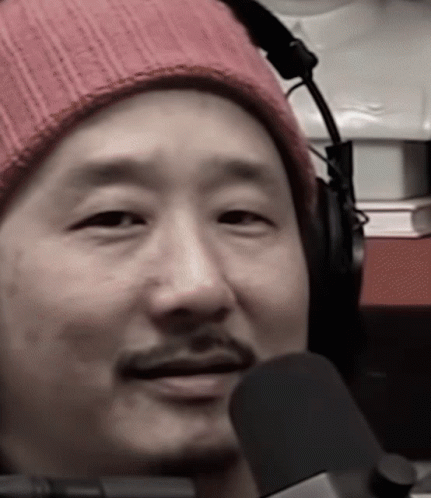 A Man Wearing Headphones And A Pink Beanie Looks At The Camera GIF