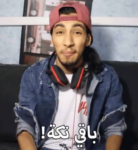 A Man Wearing Headphones And A Pink Nike Hat Is Sitting On A Couch And Making A Funny Face GIF