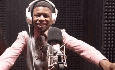 A Man Wearing Headphones And A Pink Shirt Is Standing In Front Of A Microphone GIF