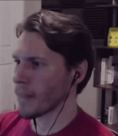 A Man Wearing Headphones And A Red Shirt Is Looking At The Camera . GIF