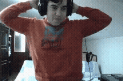 A Man Wearing Headphones And A Red Sweater Is Standing In A Room . GIF