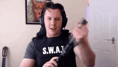 A Man Wearing Headphones And A S.w.a.t Vest Is Holding A Gun In His Hand . GIF