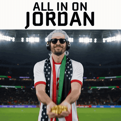 A Man Wearing Headphones And A Scarf Is Holding Gold In Front Of A Stadium That Says All In On Jordan GIF