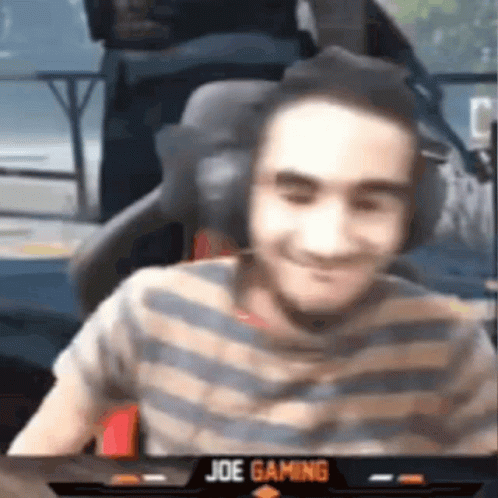 A Man Wearing Headphones And A Striped Shirt Is Smiling While Sitting In A Chair . GIF