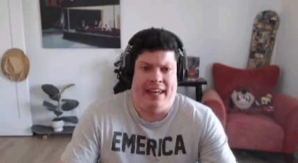 A Man Wearing Headphones And A T-Shirt That Says Emerica Is Sitting In A Living Room . GIF
