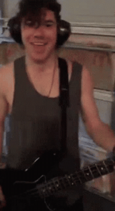 A Man Wearing Headphones And A Tank Top Is Holding A Guitar GIF