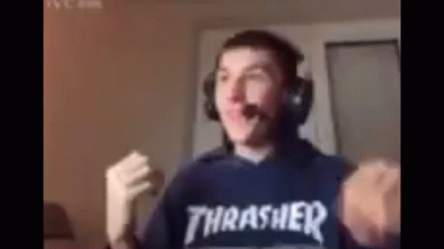 A Man Wearing Headphones And A Thrasher Shirt Is Standing In Front Of A Computer . GIF