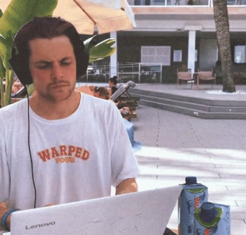 A Man Wearing Headphones And A Warped T-Shirt Is Typing On A Lenovo Laptop GIF