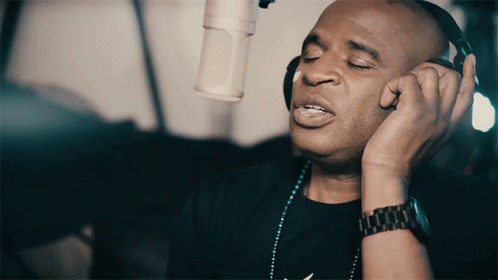 A Man Wearing Headphones And A Watch Sings Into A Microphone GIF