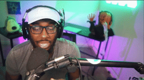 A Man Wearing Headphones And A White Hat Is Talking Into A Microphone GIF