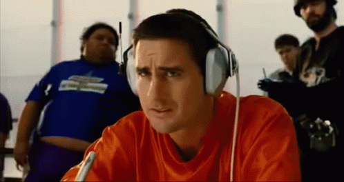 A Man Wearing Headphones And An Orange Shirt Is Looking At Something GIF