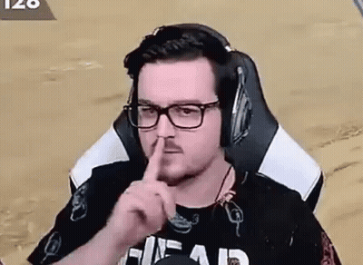 A Man Wearing Headphones And Glasses Is Sitting In A Chair And Making A Shhh Gesture . GIF