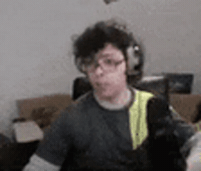 A Man Wearing Headphones And Glasses Is Sitting In A Living Room With A Cat . GIF