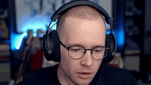A Man Wearing Headphones And Glasses Is Sitting In Front Of A Computer . GIF