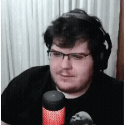 A Man Wearing Headphones And Glasses Is Sitting In Front Of A Microphone And Smiling . GIF