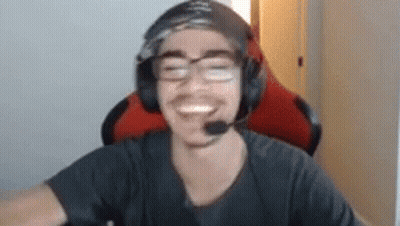 A Man Wearing Headphones And Glasses Is Smiling While Sitting In A Gaming Chair . GIF