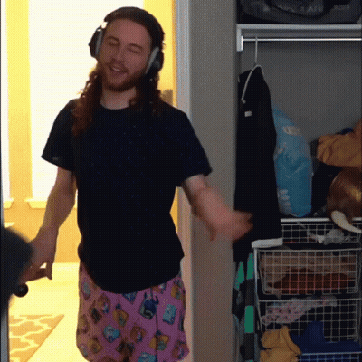 A Man Wearing Headphones And Pink Pajama Pants Is Standing In A Closet GIF