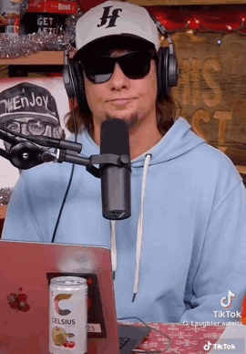 A Man Wearing Headphones And Sunglasses Is Sitting In Front Of A Microphone And A Laptop . GIF