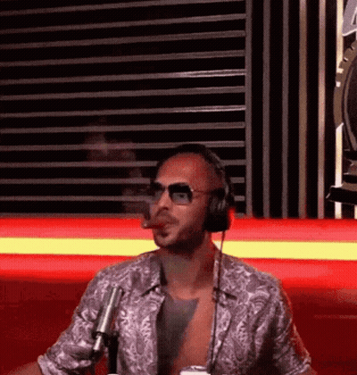 A Man Wearing Headphones And Sunglasses Is Smoking A Cigar While Sitting In Front Of A Microphone . GIF