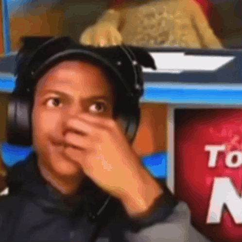 A Man Wearing Headphones Covering His Nose In Front Of A Sign That Says " To " GIF