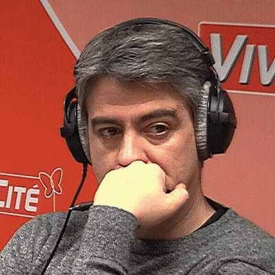 A Man Wearing Headphones Has His Hand On His Mouth In Front Of A Sign That Says Vive GIF
