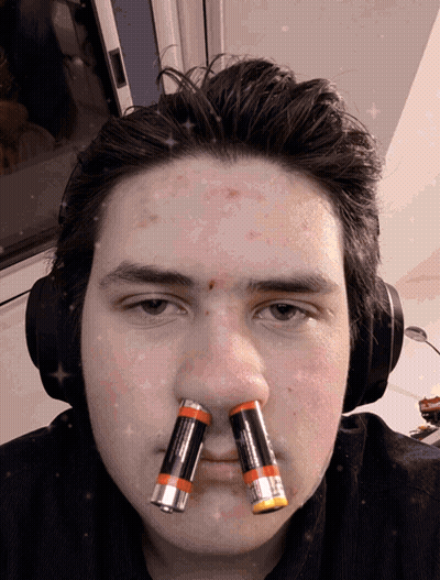 A Man Wearing Headphones Has Two Batteries On His Nose GIF