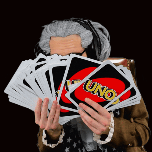 A Man Wearing Headphones Holds A Stack Of Uno Cards In Front Of His Face GIF