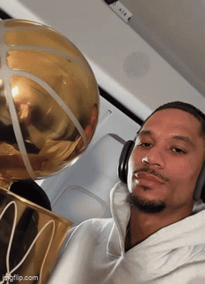 A Man Wearing Headphones Is Holding A Basketball Trophy With The Letter M On It GIF