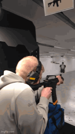 A Man Wearing Headphones Is Holding A Gun In A Shooting Range .. GIF